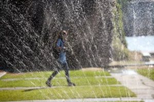 A girl is walking on a green lawn that is watering by sprinkler system