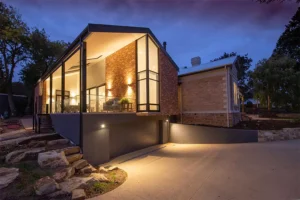 Modern home with outdoor lighting installation, featuring warm lights illuminating the exterior and pathway, enhancing nighttime curb appeal.