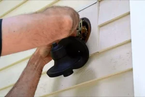 Person installing an outdoor light fixture on the exterior wall of a home for enhanced safety and functionality.