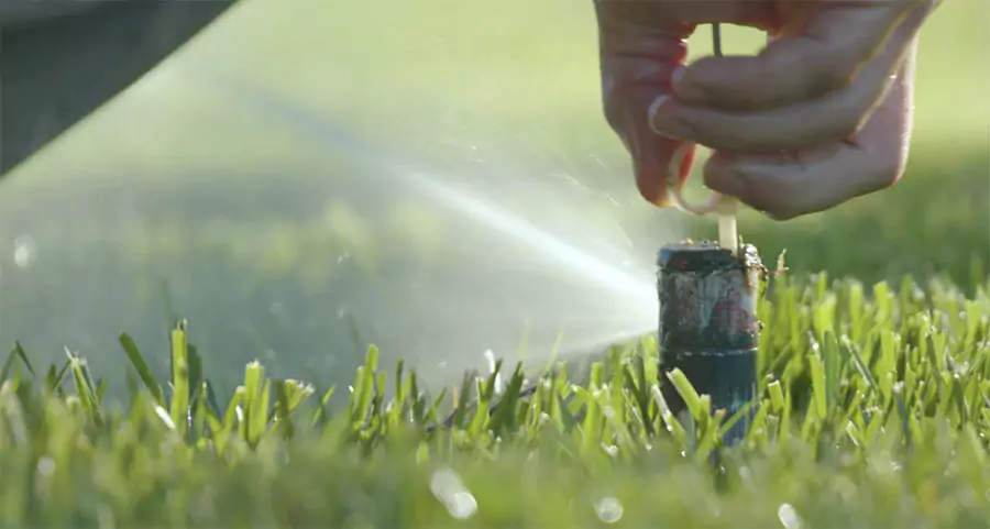 Close-up of a sprinkler head being adjusted during summer lawn irrigation maintenance in Humble, TX