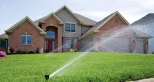 Lawn sprinkler system watering a lush green yard in front of a brick home—illustrating efficient irrigation system use for summer lawn care in Humble, TX.